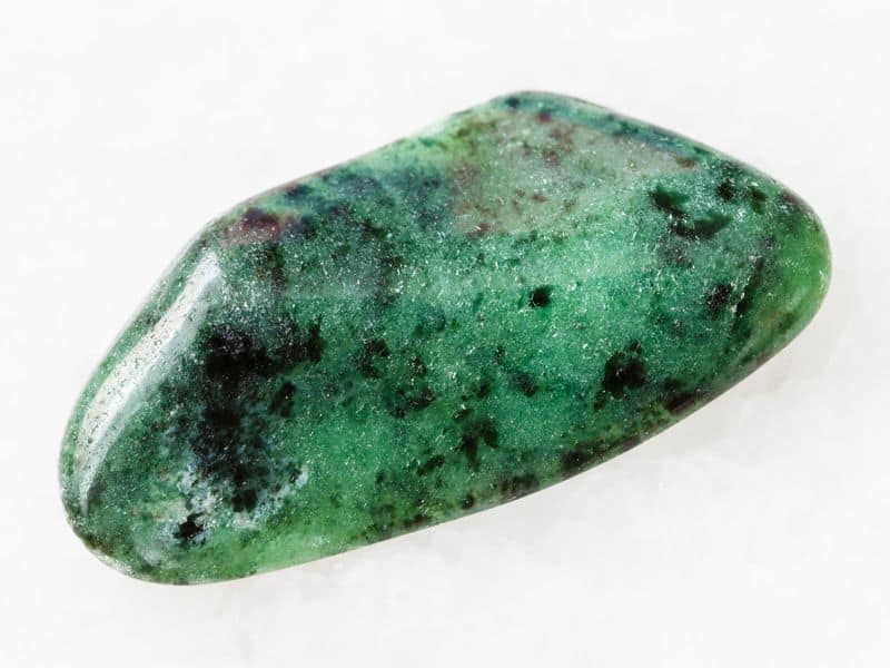 macro shooting of natural mineral rock specimen - polished zoisite gemstone on white marble 