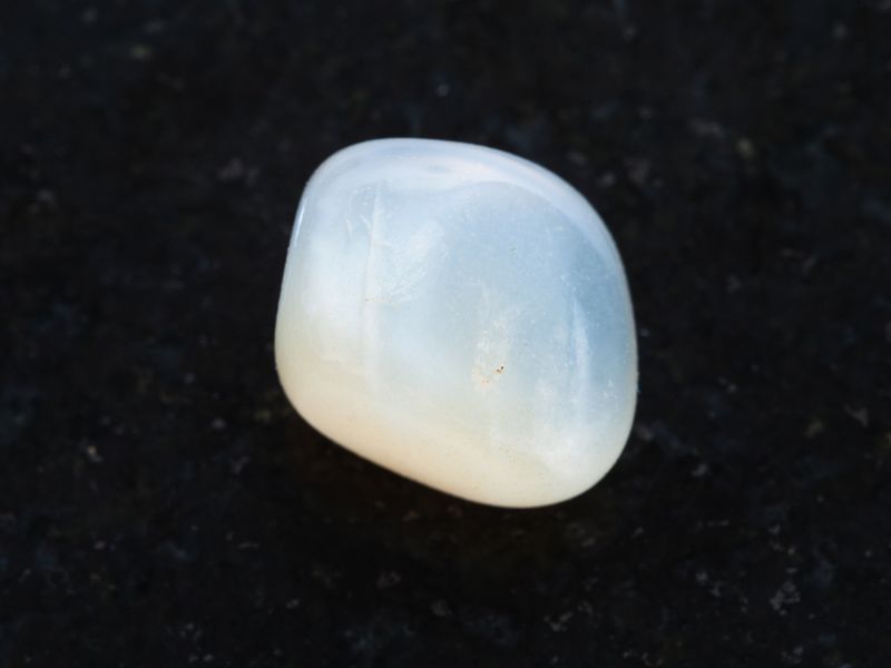 macro shooting of natural mineral rock specimen - tumbled translucent moonstone gemstone on dark granite background